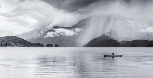 Man sitting on boat in lake against mountains