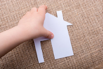 Close-up of human hand holding white cardboard house on burlap