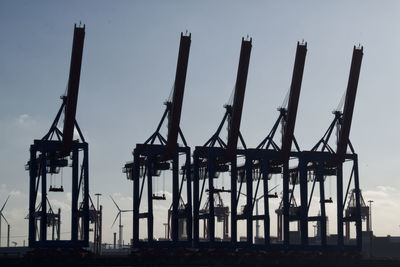 Silhouette of cranes at harbor against sky