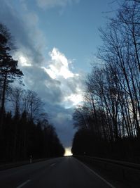 Road amidst silhouette trees against sky