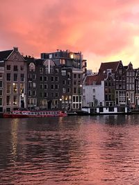 Buildings by river against sky during sunset
