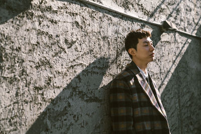 Young man looking away while standing against wall