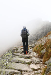 Rear view of hiker walking on rocky mountain during foggy weather