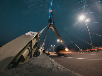 Illuminated road by bridge against sky at night