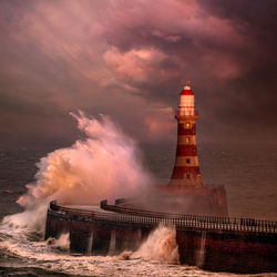 Lighthouse by sea against sky during sunset