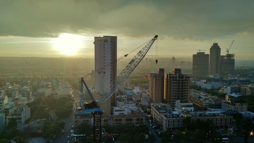 Crane and buildings in city during sunset