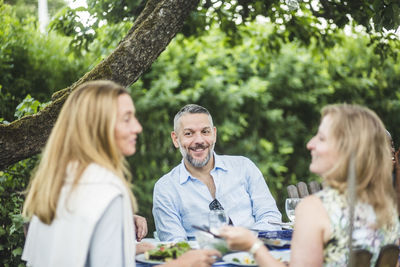 Smiling mature man looking at female friends while enjoying garden party during weekend