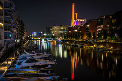 Boats moored in illuminated city against sky at night