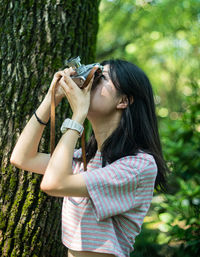 Young woman using phone while standing on tree