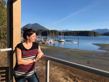 Woman looking away while standing by railing against blue sky