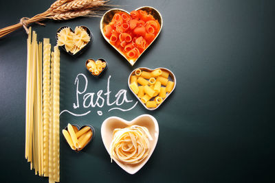 Close-up of heart shape containers with raw pastas and text on black background