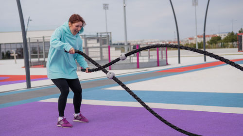 Full length of woman exercising battle rope outside