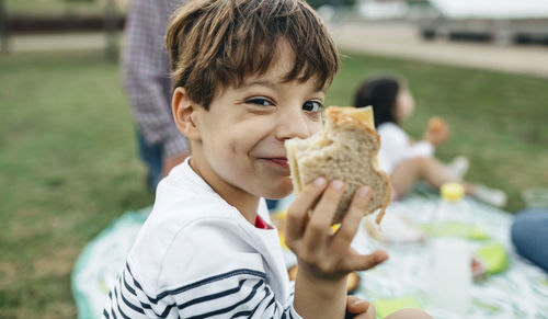 Portrait of smiling boy holding sandwich with his family in background