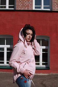 Young woman standing against red building