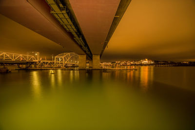 Illuminated bridge over river in city against sky at night