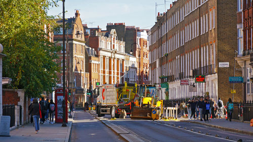 People walking on road by buildings in city