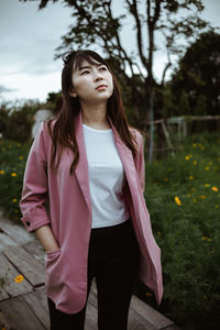 Young woman looking away while standing against tree