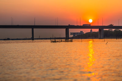 Bridge over sea against orange sky