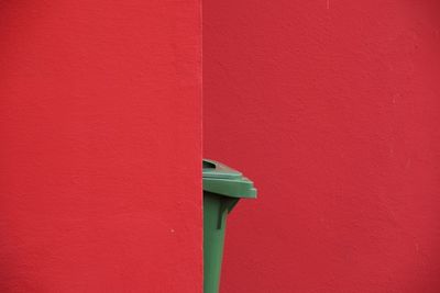 Close-up of green carbage bin against red wall