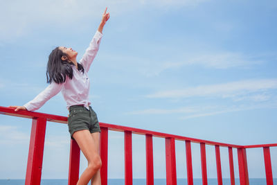 Woman with umbrella on railing against sky