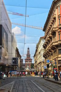 People on city street amidst buildings against sky