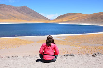 Rear view of woman sitting on sand against mountain