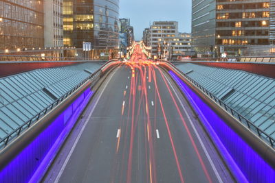 Light trails on street amidst buildings in city at dusk