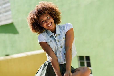 Portrait of cheerful of young woman with curly hair against green wall