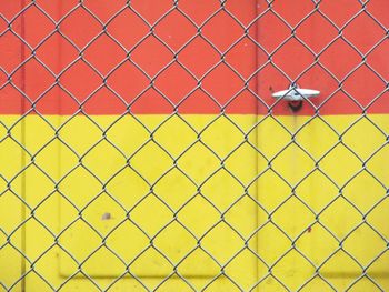 Full frame shot of yellow chainlink fence against wall