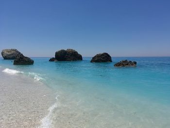 Rocks in sea against clear blue sky