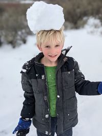 Portrait of boy standing in snow with a large snowball balancing on his head