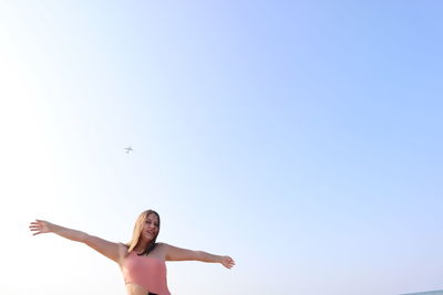 Low angle view of woman with airplane flying against clear sky