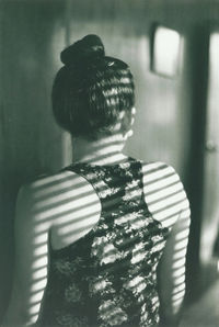 Rear view of woman standing against wall at home