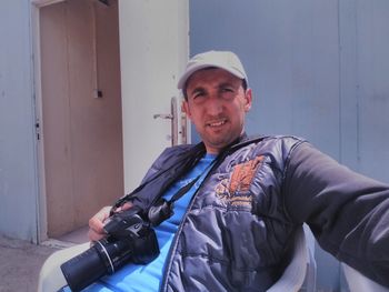 Man with camera sitting on chair against open door