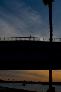 Silhouette bridge over river against sky during sunset