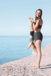 Portrait of smiling woman holding daughter at beach against sky