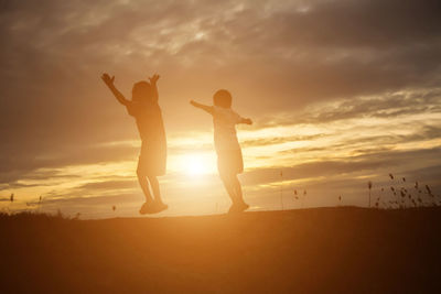 Silhouette friends standing on land against sky during sunset