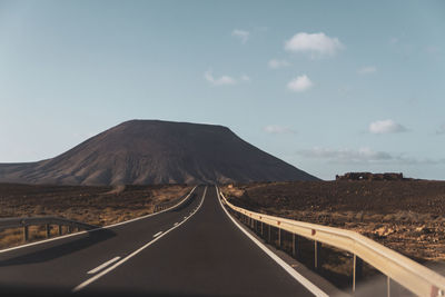 Empty road leading towards mountains against sky