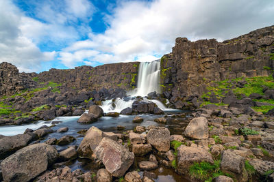 Scenic view of waterfall on rocks against sky