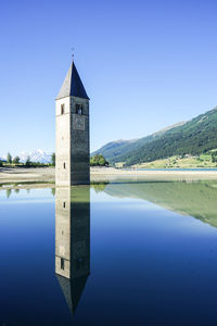 Tower by lake against clear blue sky