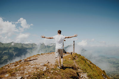 Rear view of man standing on mountain against sky