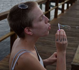 High angle view of young woman blowing bubble on pier over lake
