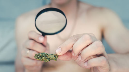 Midsection of man holding medical cannabis and magnifying glass