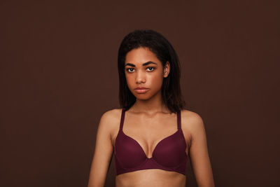 Portrait of young woman standing against black background