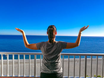 Rear view of woman with arms raised looking at sea against sky