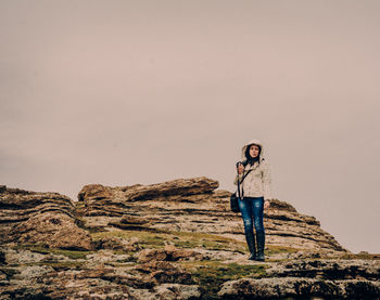 Portrait of young woman standing on rock against sky