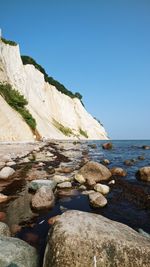 Rocks by sea against clear blue sky