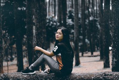 Side view of young woman sitting on tree trunk in forest