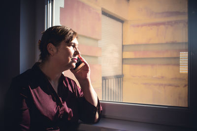 Woman talking on mobile phone while looking through window