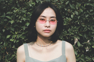 Close-up portrait of young woman wearing sunglasses standing against plants